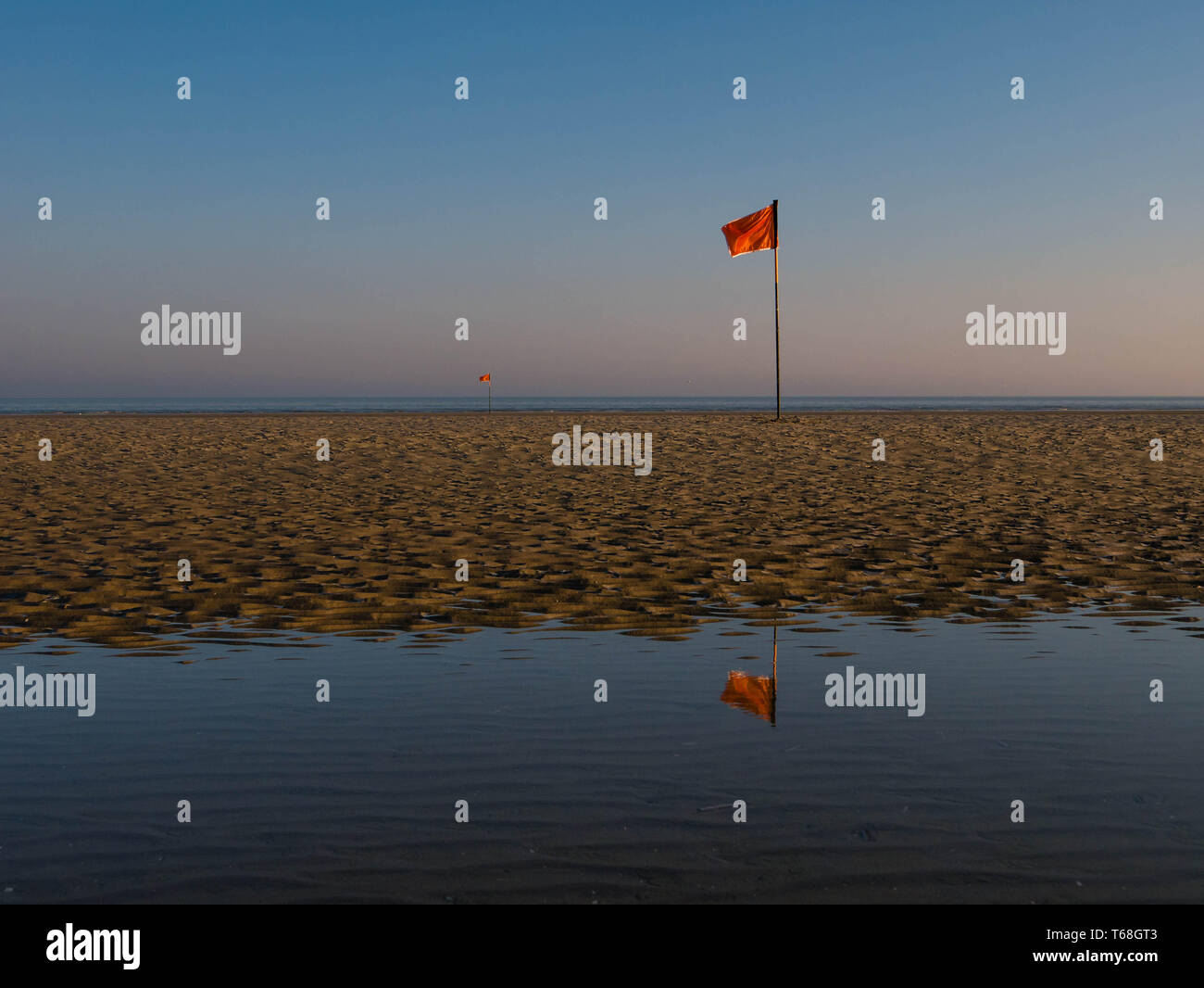 Red flag mirroring in water during morning hours at a beach in northern France Stock Photo