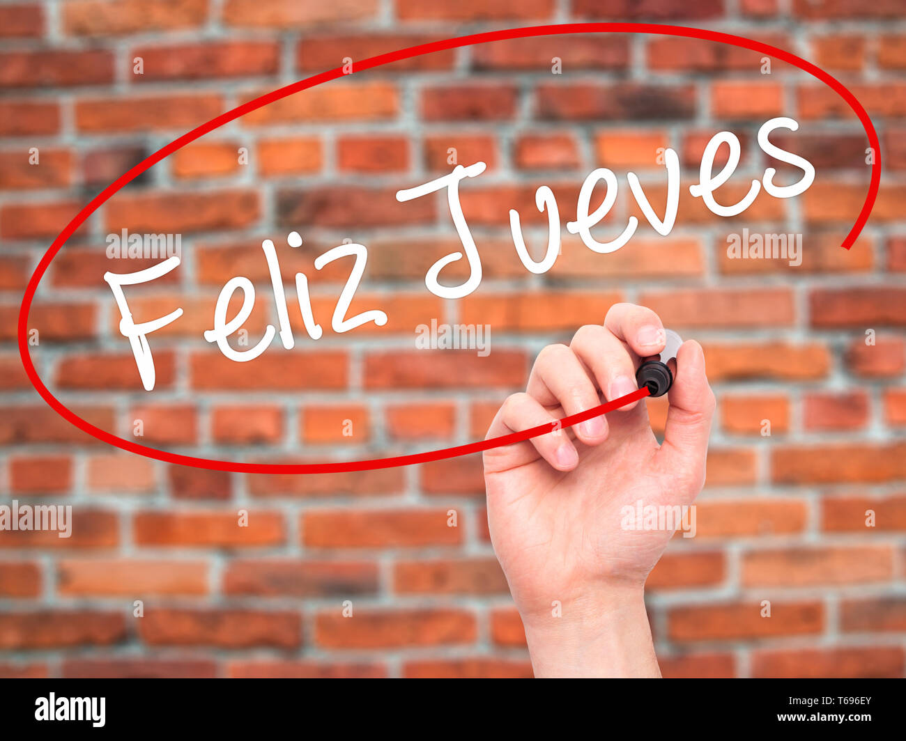 Man Hand writing Feliz Jueves (Happy Thursday In Spanish) with black