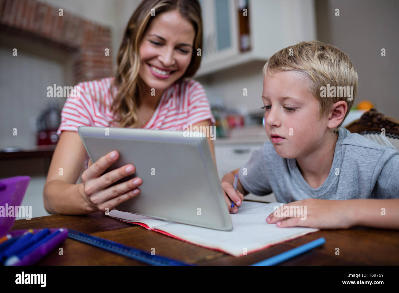 Mother using a digital tablet while helping son with his homework Stock Photo