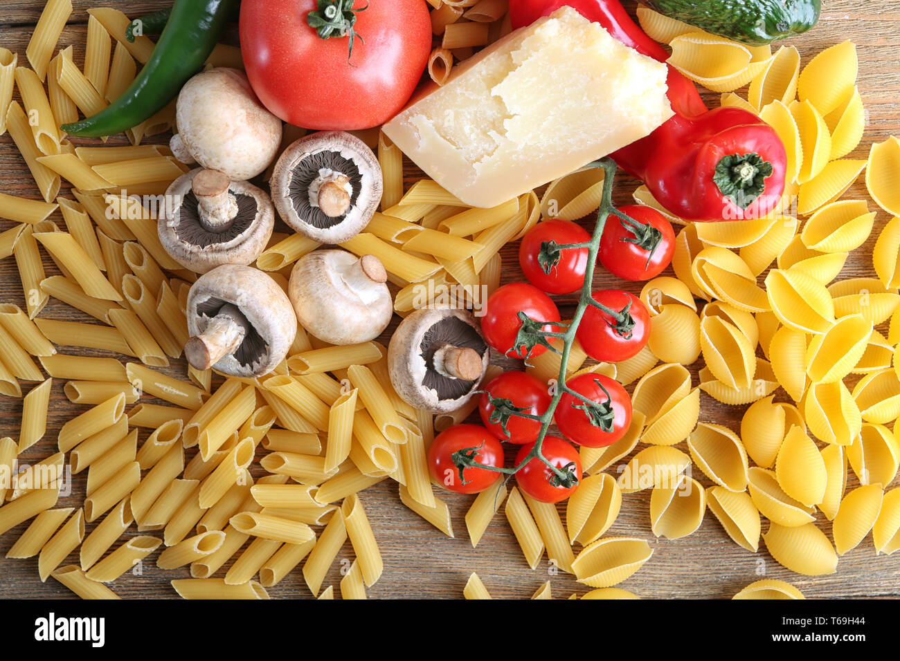 Different raw pasta with vegetables and cheese on table Stock Photo