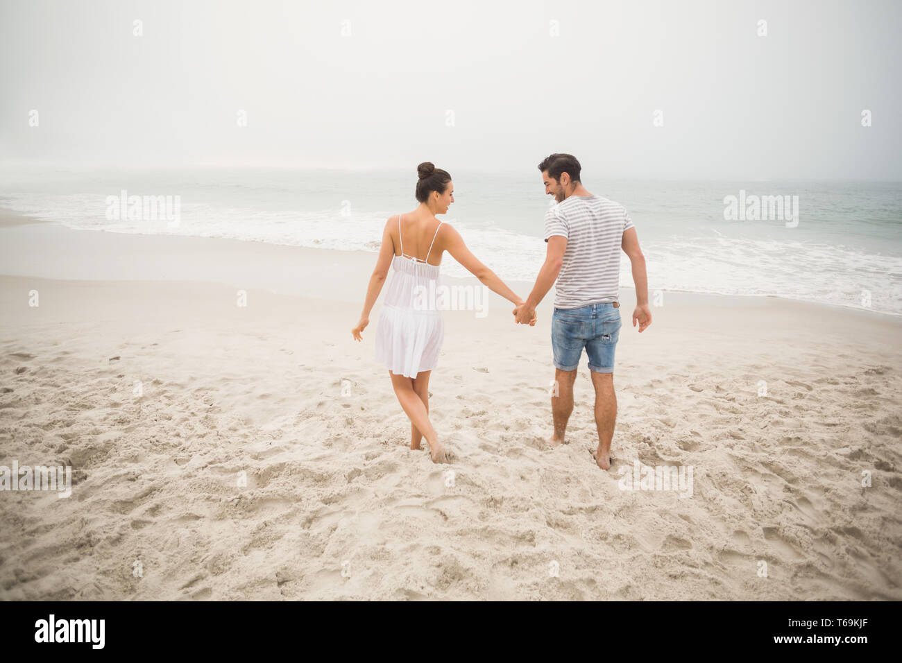 Rear view of couple holding hands and walking on the beach Stock Photo ...