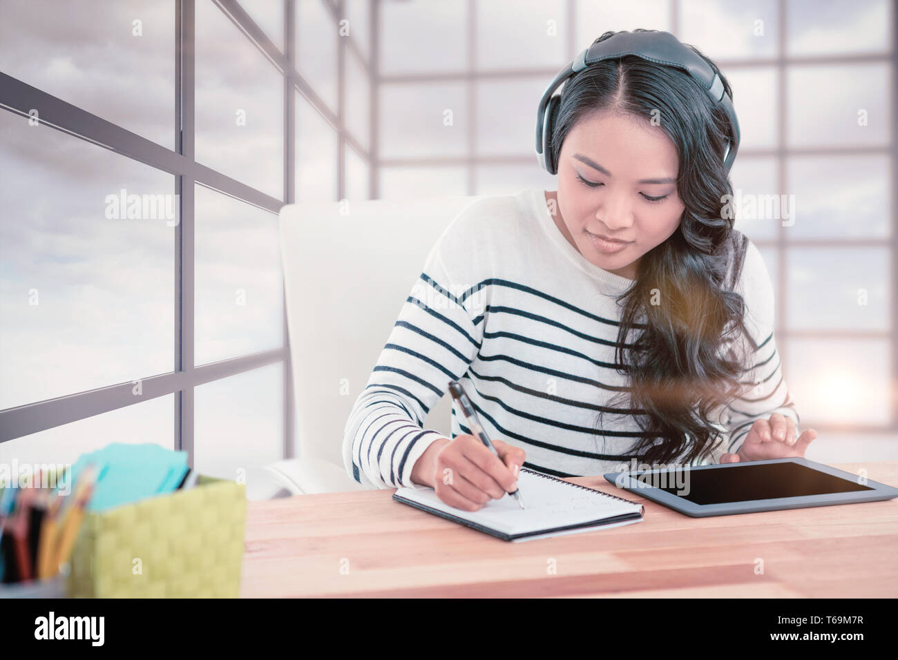 Composite image of smiling asian woman with headphones writing on notepad Stock Photo