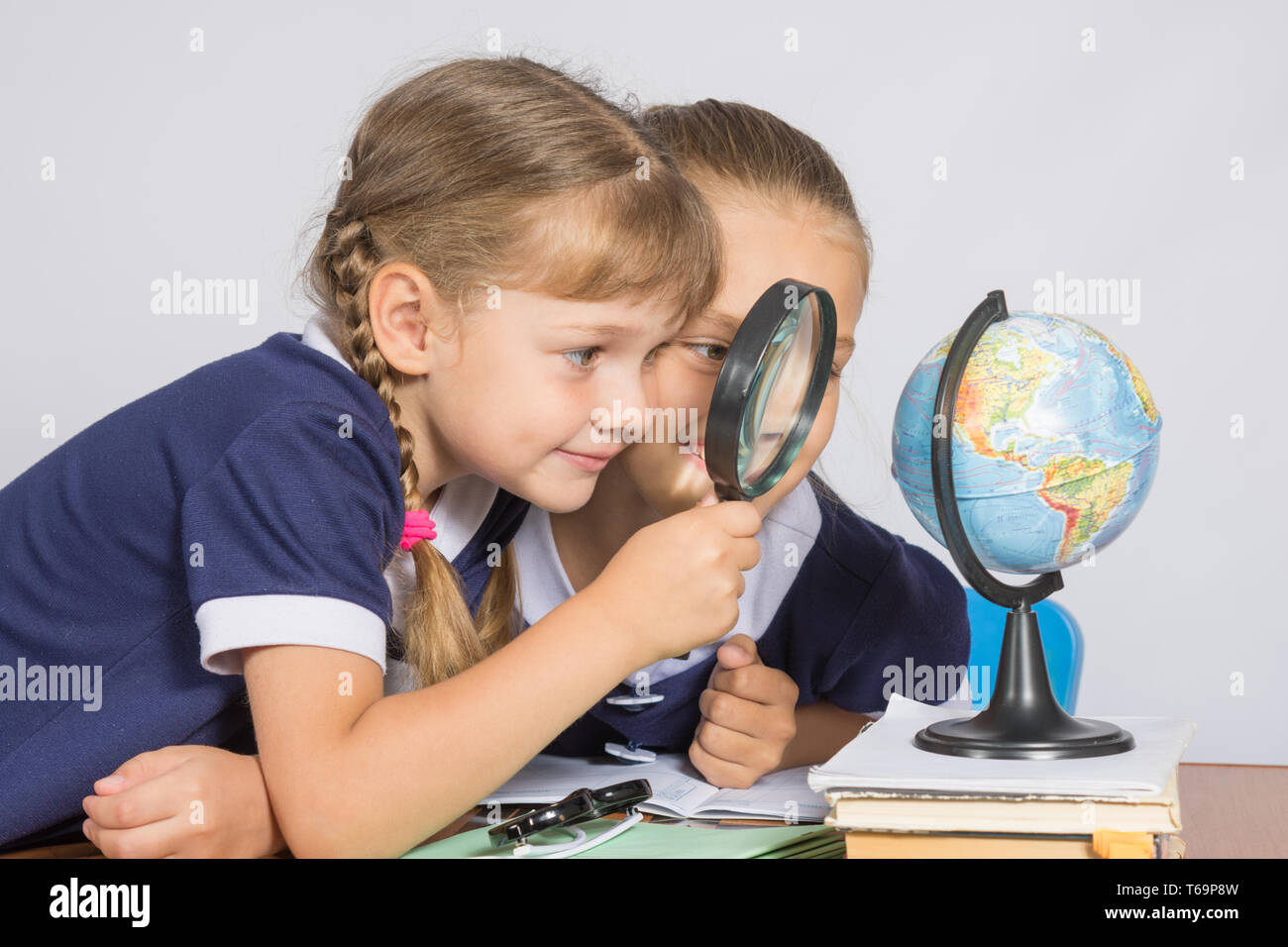 Two girls girlfriends looking at globe through a magnifying glass Stock Photo