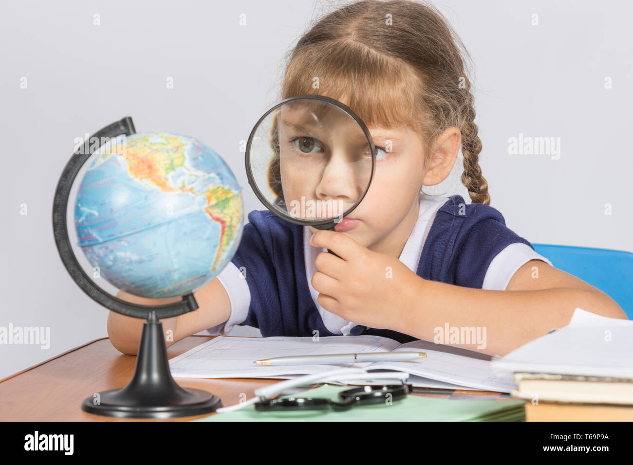 Schoolgirl looking at globe through a magnifying glass Stock Photo