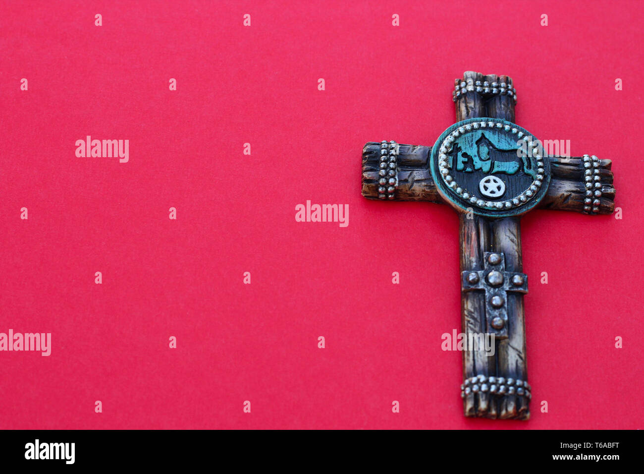 western resin cross with a horse laying flat on a red background with copy space Stock Photo