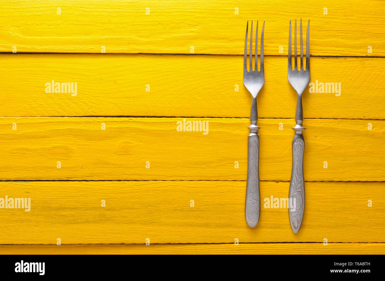 Two antique forks on a wooden table in yellow. Top view. Copy space. Stock Photo