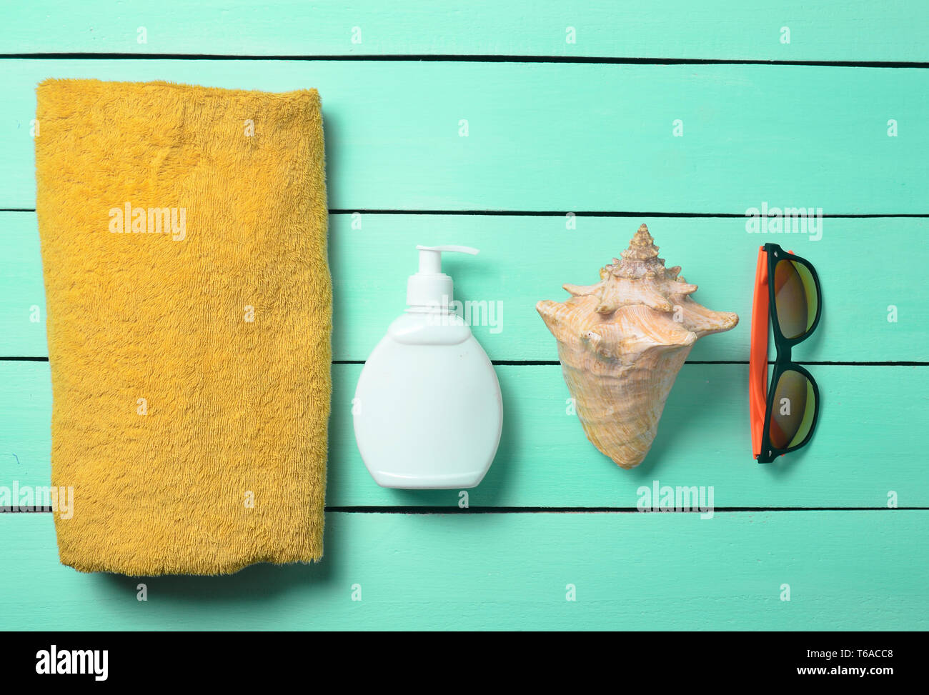 Products and accessories for relaxing on the beach: sunblock, towel, sunglasses, shell on a turquoise wooden background. The concept of the resort. Stock Photo