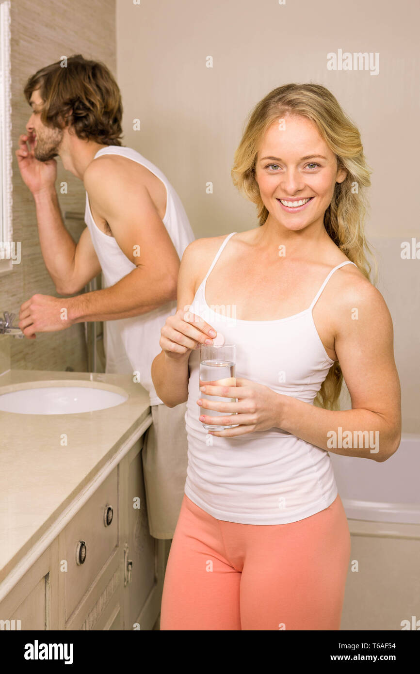 Blonde woman taking a pill with her boyfriend brushing his teeth Stock Photo