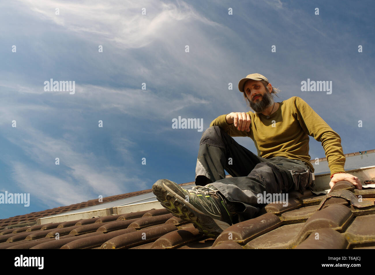 bearded roofer resting on top of a roof sunny day Stock Photo