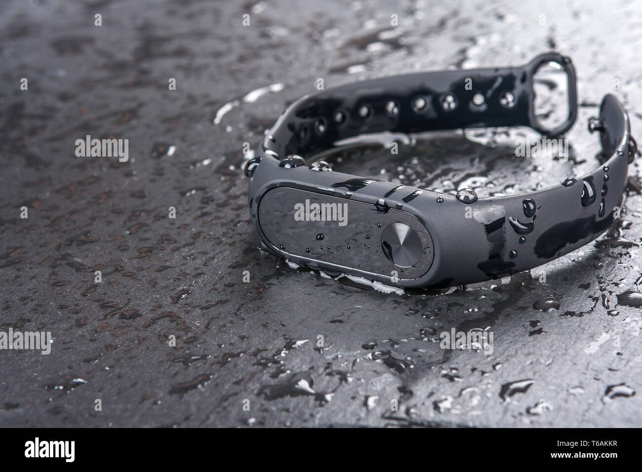 wet fitness bracelet, fitness tracker on a black slate background with drops of water Stock Photo