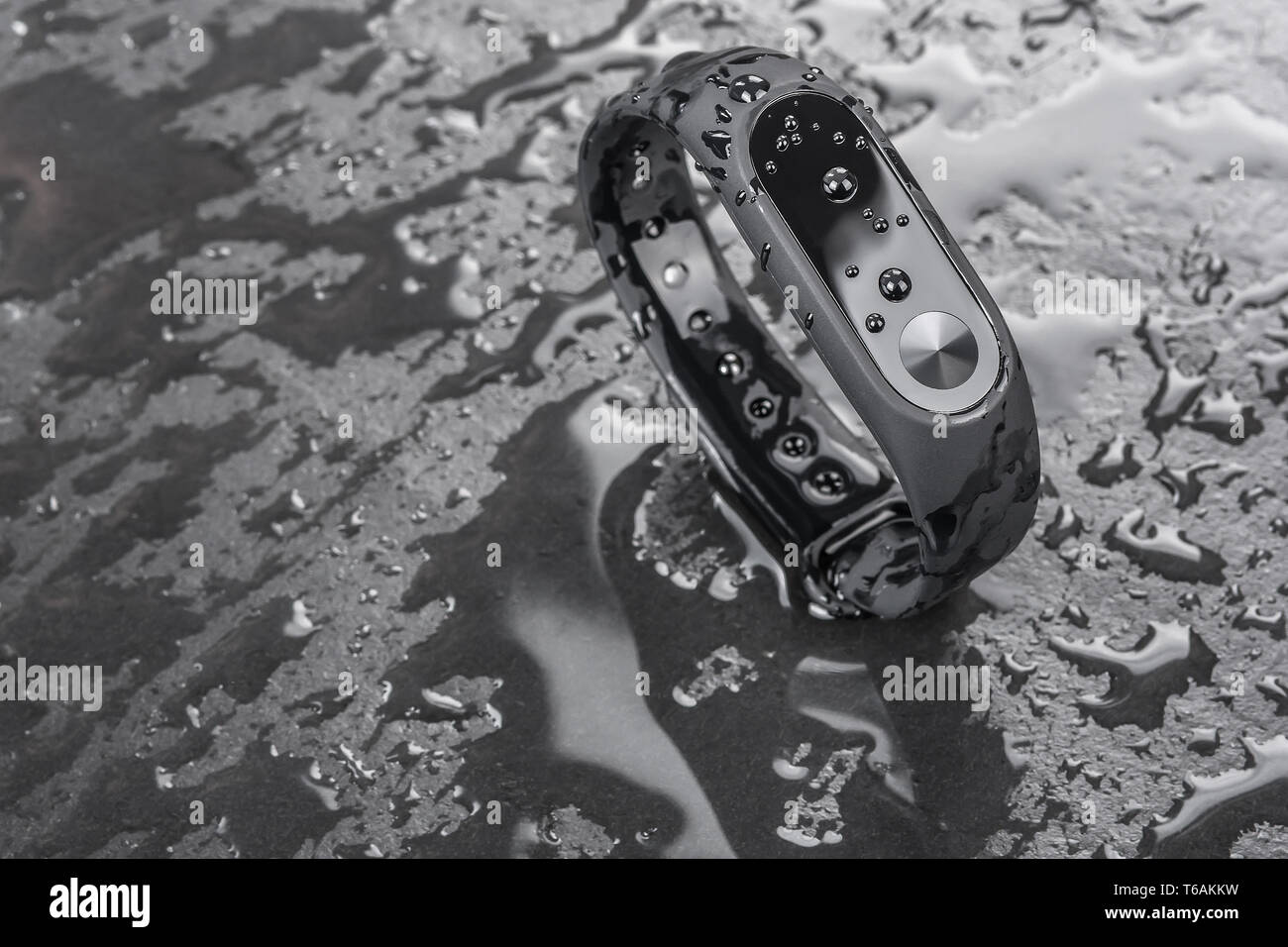 wet fitness bracelet, fitness tracker on a black slate background with drops of water Stock Photo