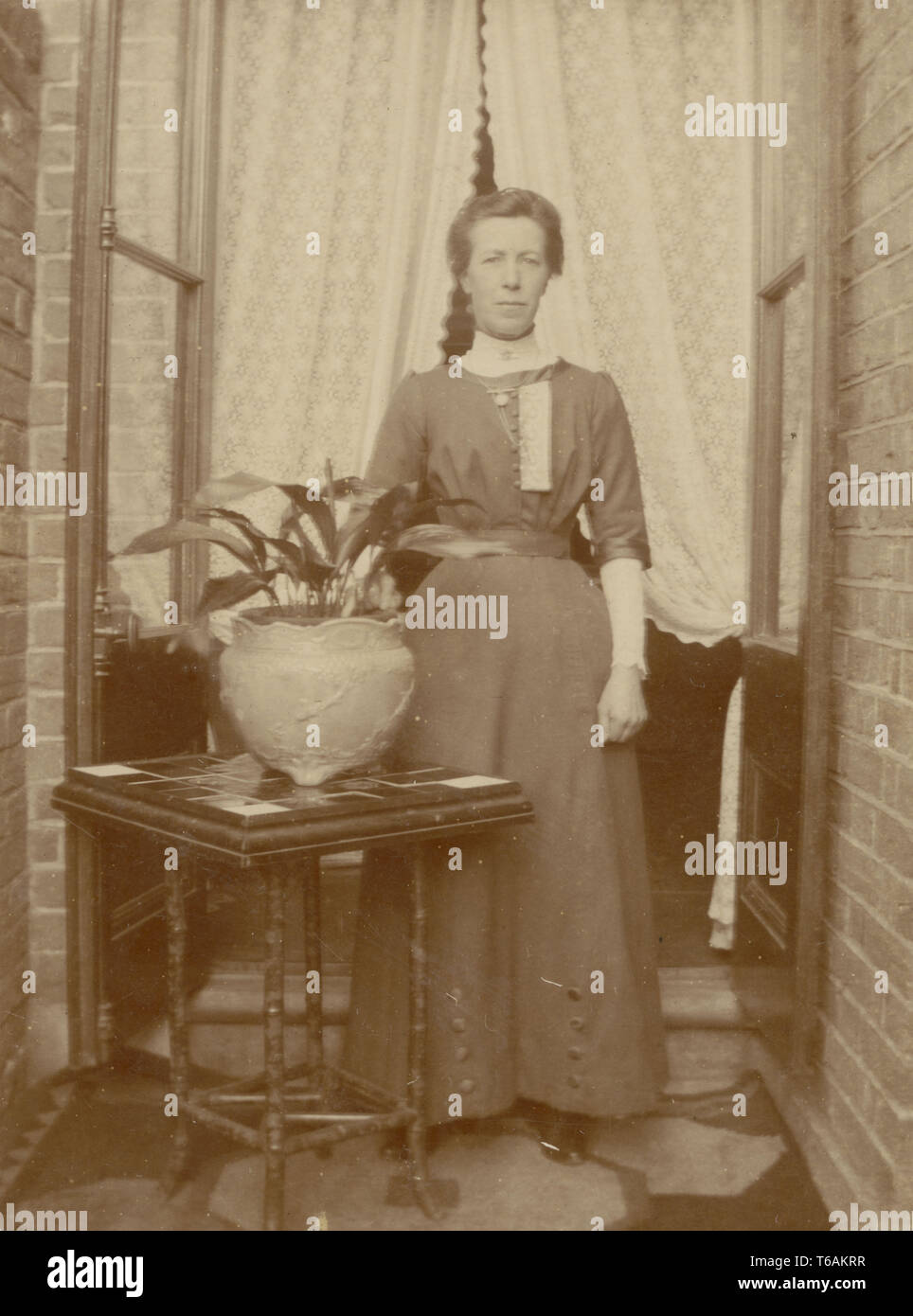 Edwardian postcard of woman outside house with Aspidistra house plant in pot, U.K. circa 1910 Stock Photo