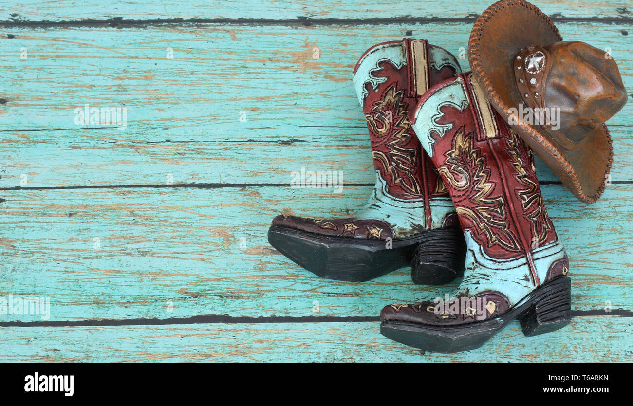 brown and blue cowboy boots and brown hat laying on a rustic blue wood background with writing space Stock Photo
