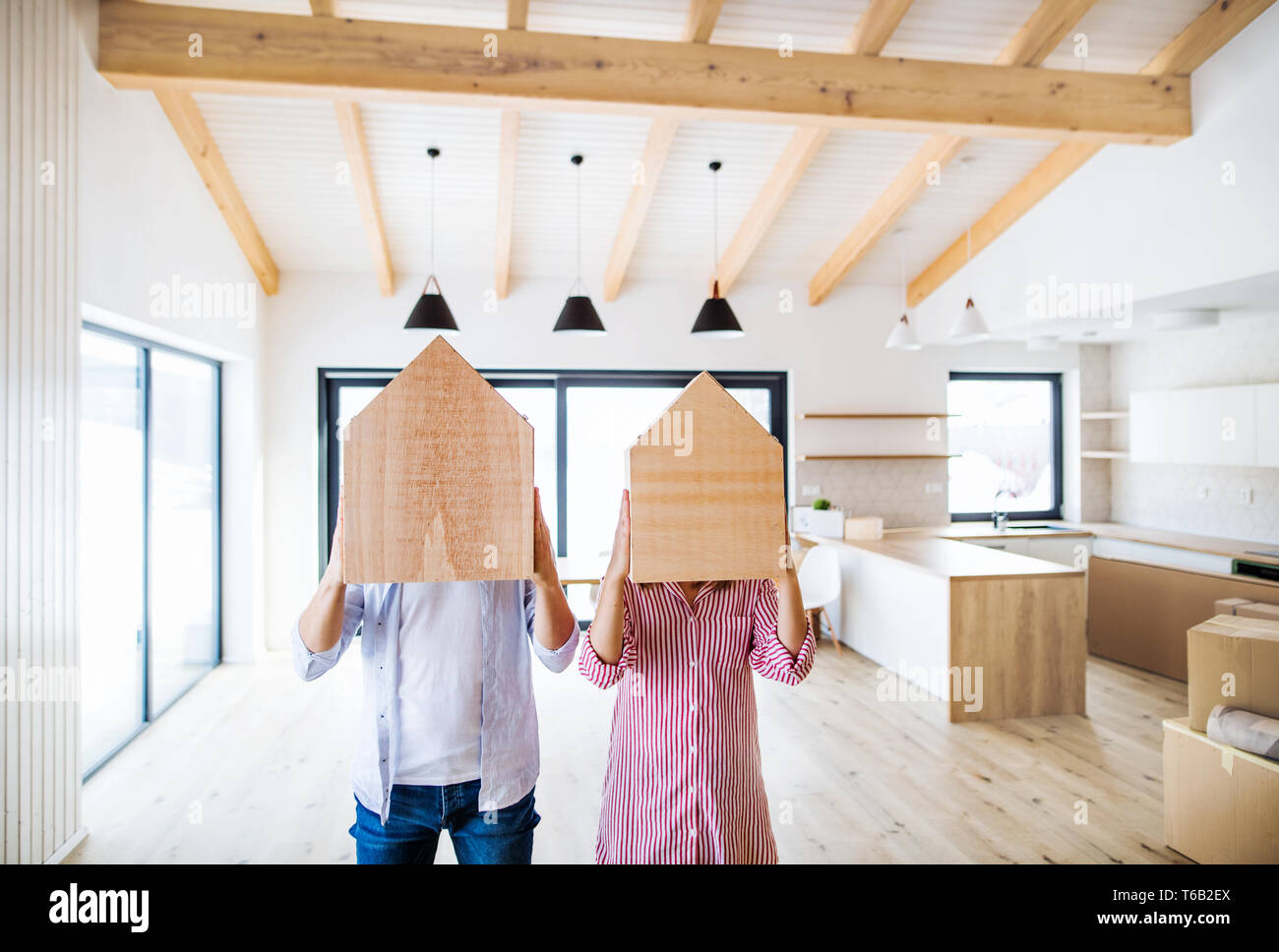 A young couple covering faces with wooden house. A moving in new home concept. Copy space. Stock Photo