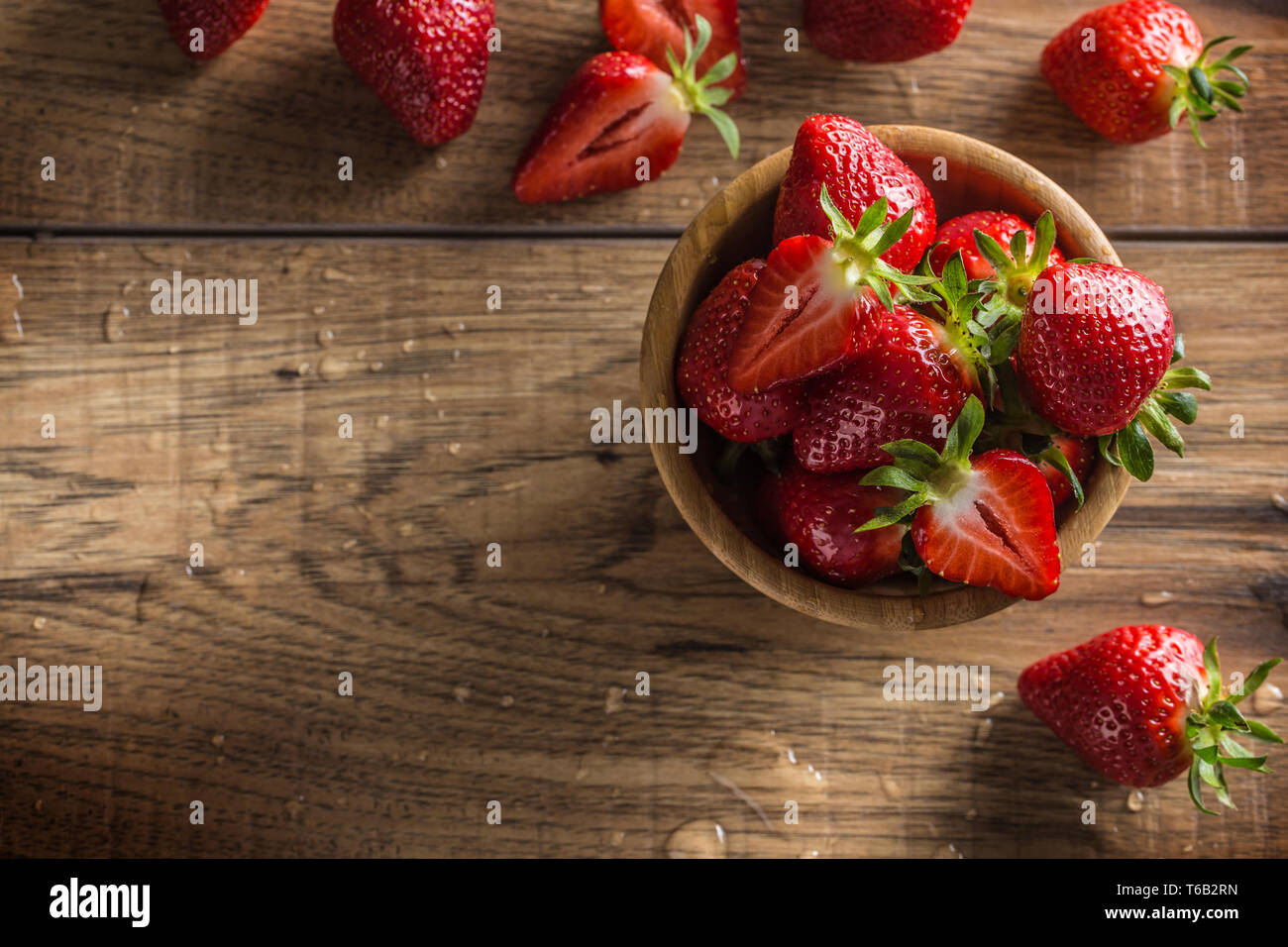 Juicy washed strawberries in wooden bowl on kitchen table Stock Photo