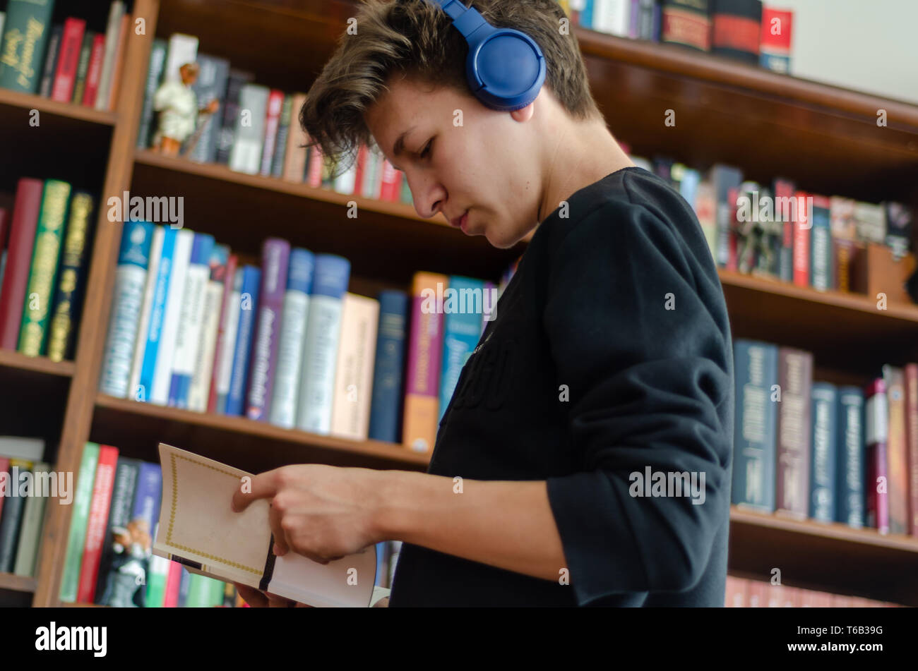 The teenage listens to music and reads book in front of library at home Stock Photo