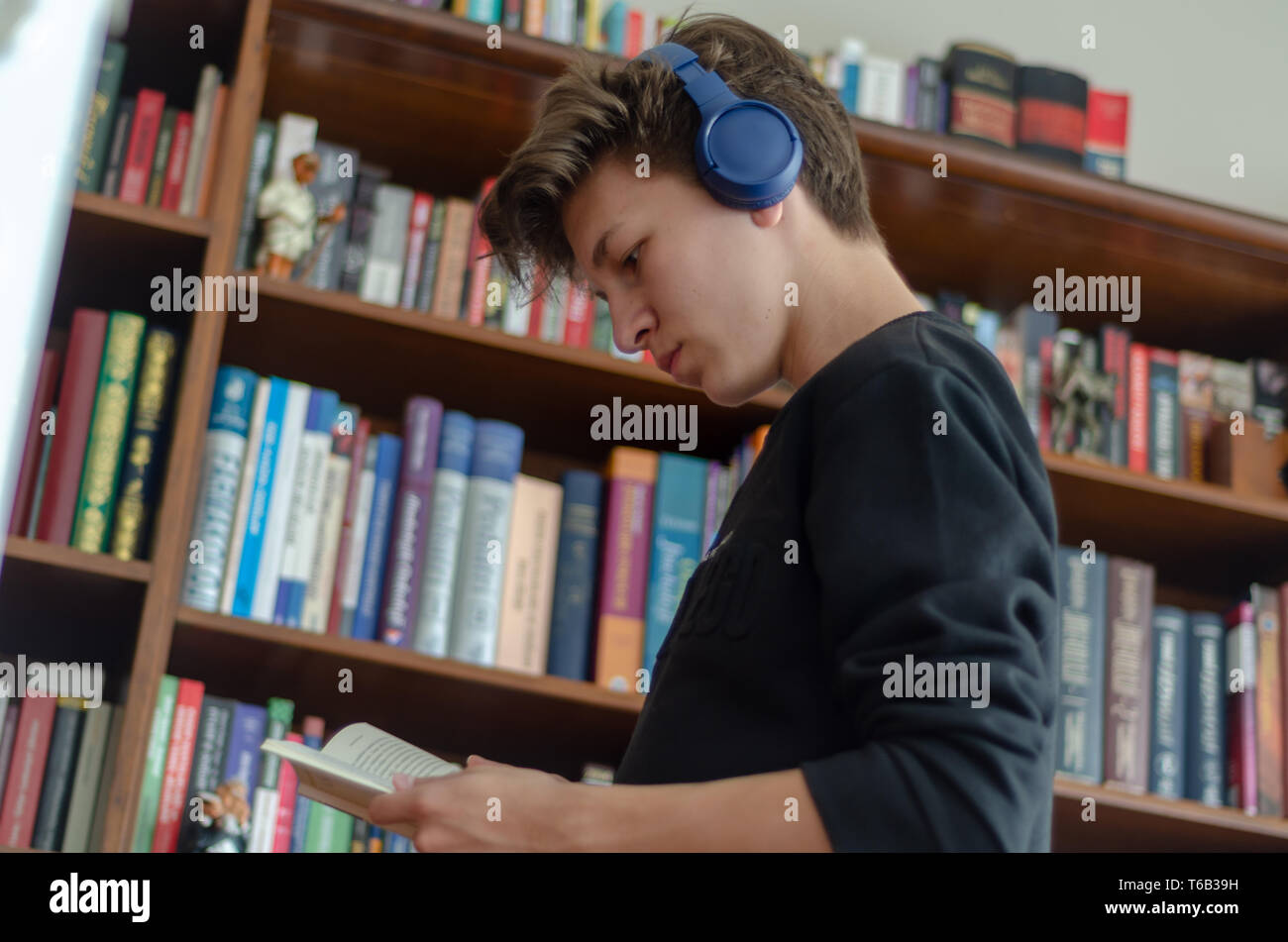 The teenage listens to music and reads book in front of library at home Stock Photo