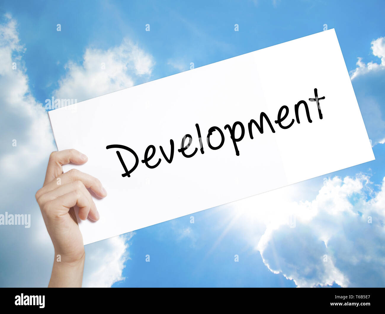 Development Sign on white paper. Man Hand Holding Paper with text. Isolated on sky background Stock Photo