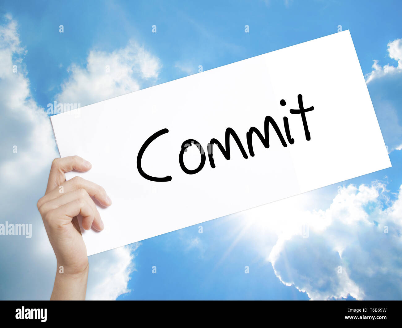 Commit Sign on white paper. Man Hand Holding Paper with text. Isolated on sky background Stock Photo