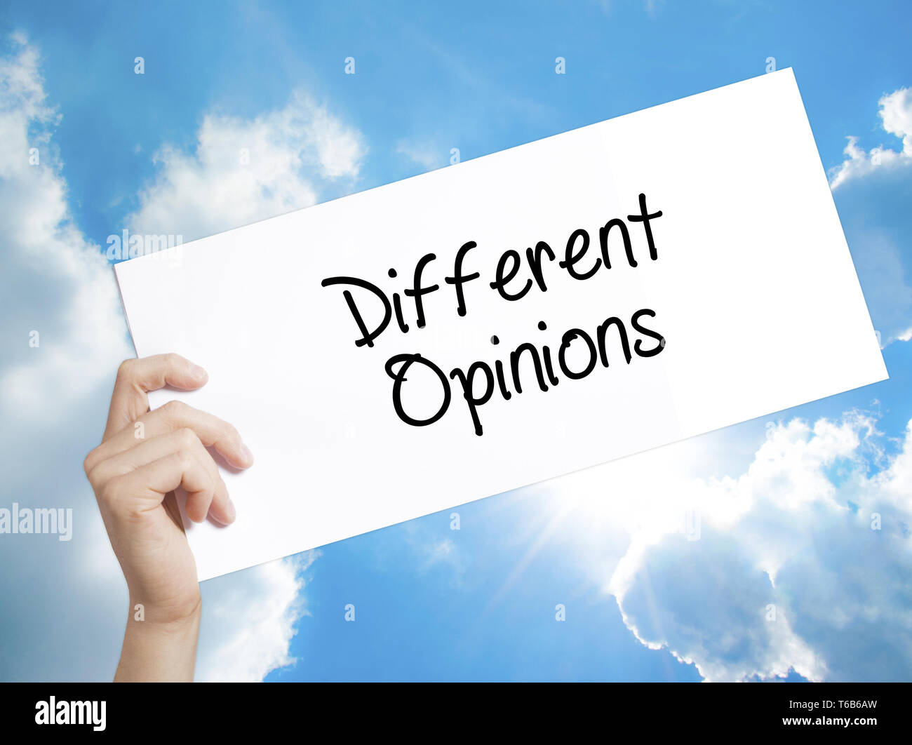 Different Opinions Sign on white paper. Man Hand Holding Paper with text. Isolated on sky background. Stock Photo