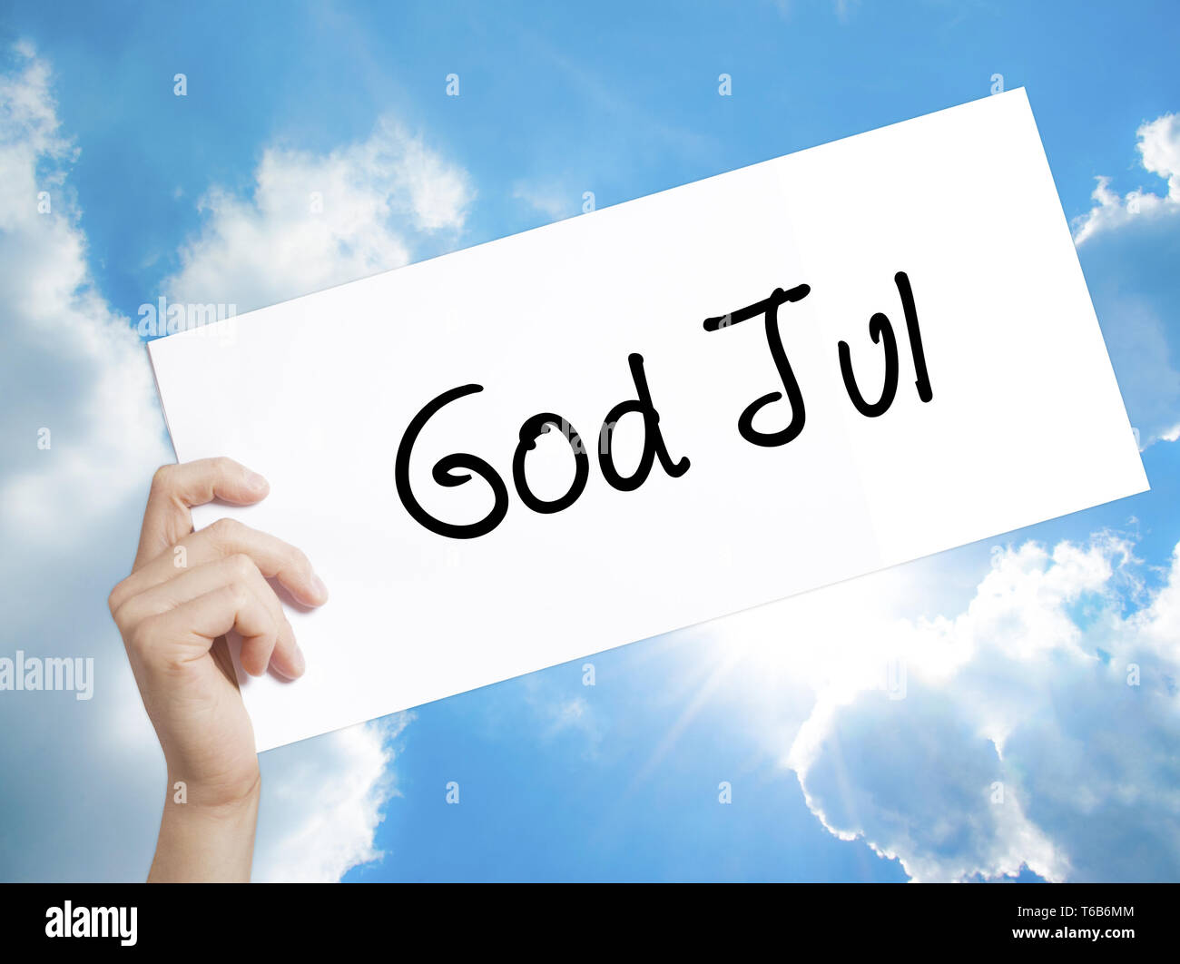 God Jul  (Merry Christmas in Swedish) Sign on white paper. Man Hand Holding Paper with text. Isolated on sky background Stock Photo