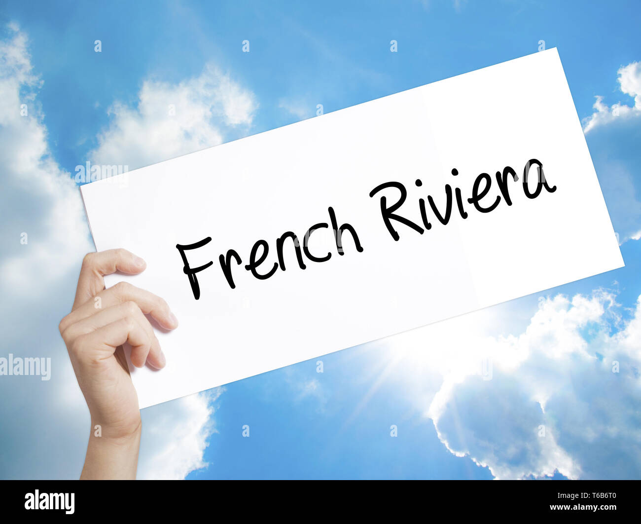 French Riviera Sign on white paper. Man Hand Holding Paper with text. Isolated on sky background Stock Photo