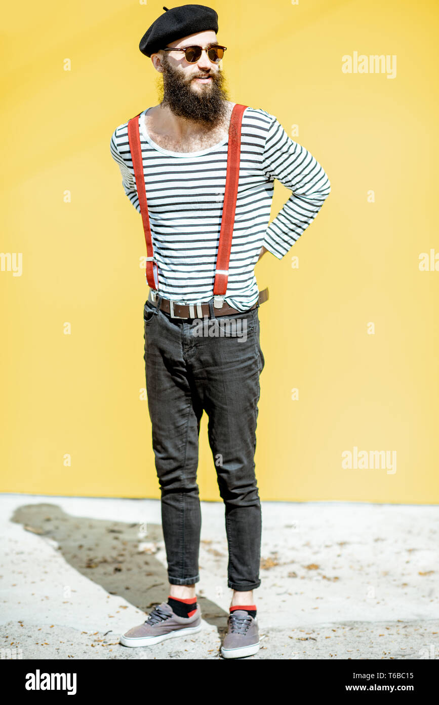 Portrait of a stylish bearded man dressed in striped shirt, suspenders and  hat on the yellow background outdoors Stock Photo - Alamy