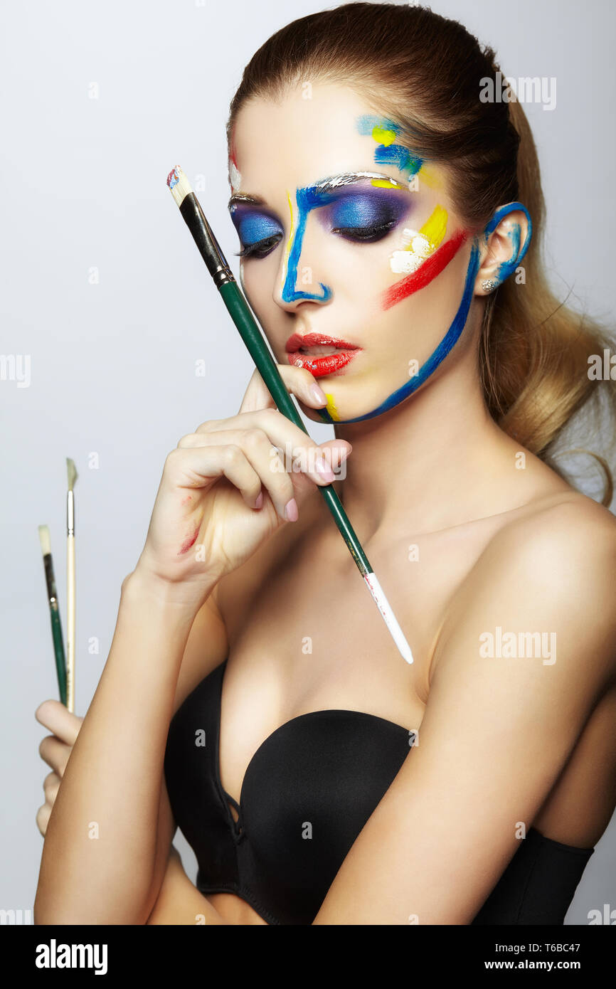 Young female painter with paint brush in hand and acrylic paint on face