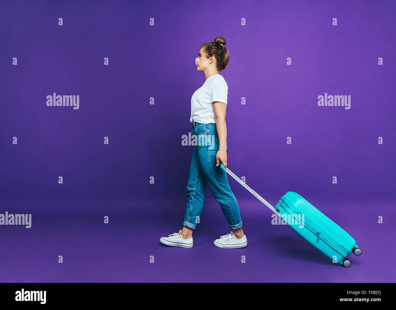 Young traveler woman in summer casual clothes is rolling a suitcase on wheels Stock Photo