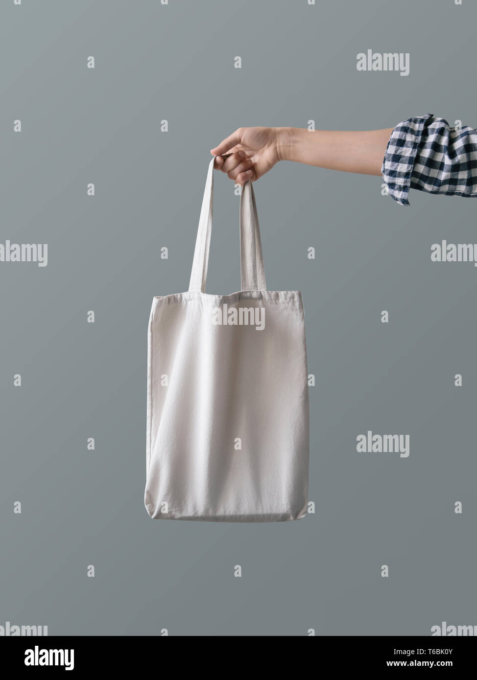 Eco-friendly product Zero waste concept A girl is holding a white blank canvas tote bag against a gray wall background Stock Photo