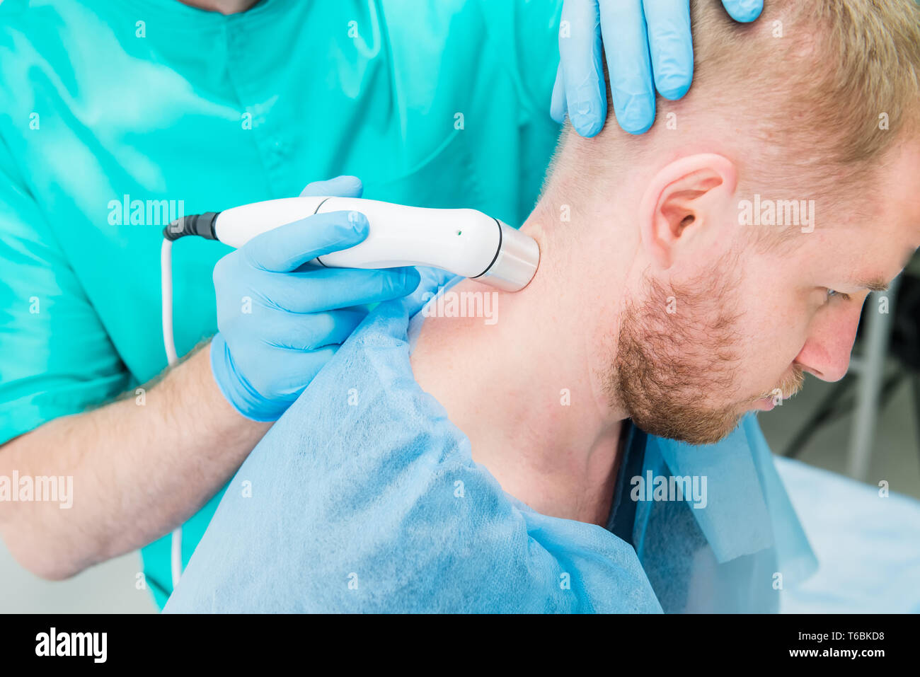Young man at the physiotherapy receiving laser therapy massage. A chiropractor treats patient's cervical spine in medical office. Neurology, Osteopath Stock Photo