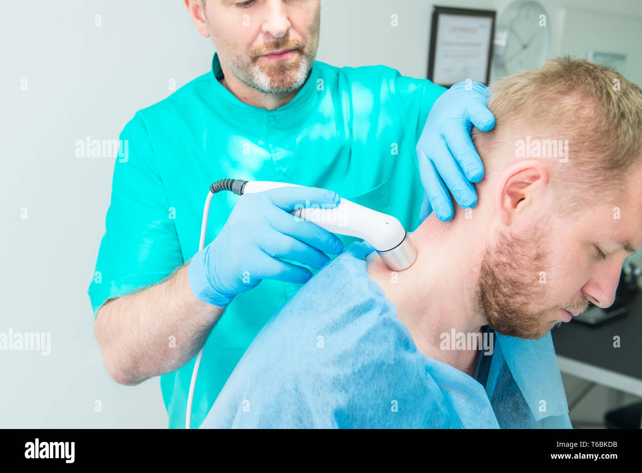 Young man at the physiotherapy receiving laser therapy massage. A chiropractor treats patient's cervical spine in medical office. Neurology, Osteopath Stock Photo