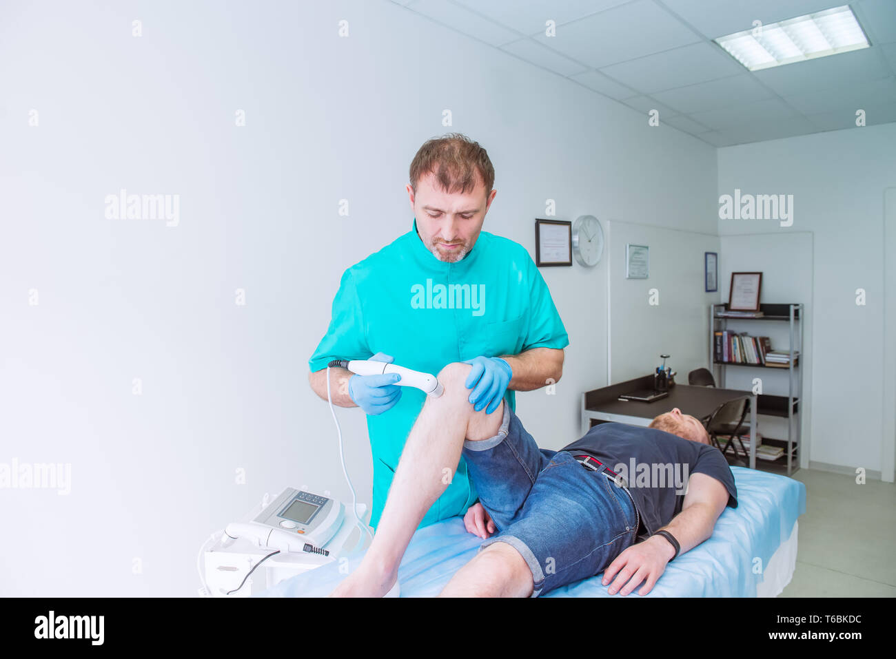 Young man receiving laser or magnet therapy massage on a knee to less pain. A chiropractor treats patient's knee-joint in medical office. Neurology, O Stock Photo