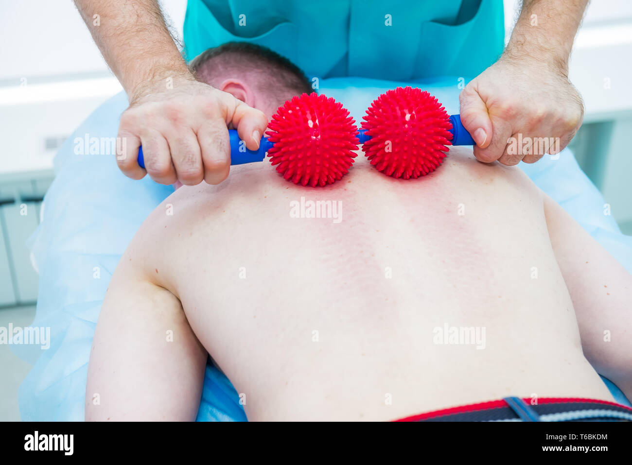Young man at the physiotherapy receiving ball massage from therapist. A chiropractor treats patient's thoracic spine in medical office. Neurology, Ost Stock Photo
