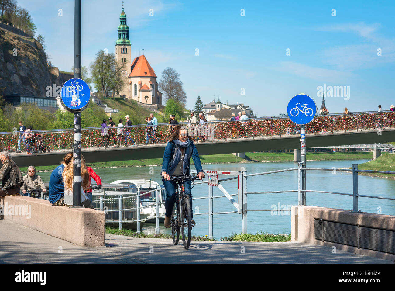 Woman cycling, view of a young woman cycling along a cycle path in the city of Salzburg with the Makartsteg bridge in the background, Austria. Stock Photo