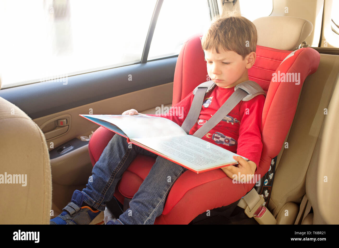 Toddler boy reading book in child car seat. Entertainment in the car