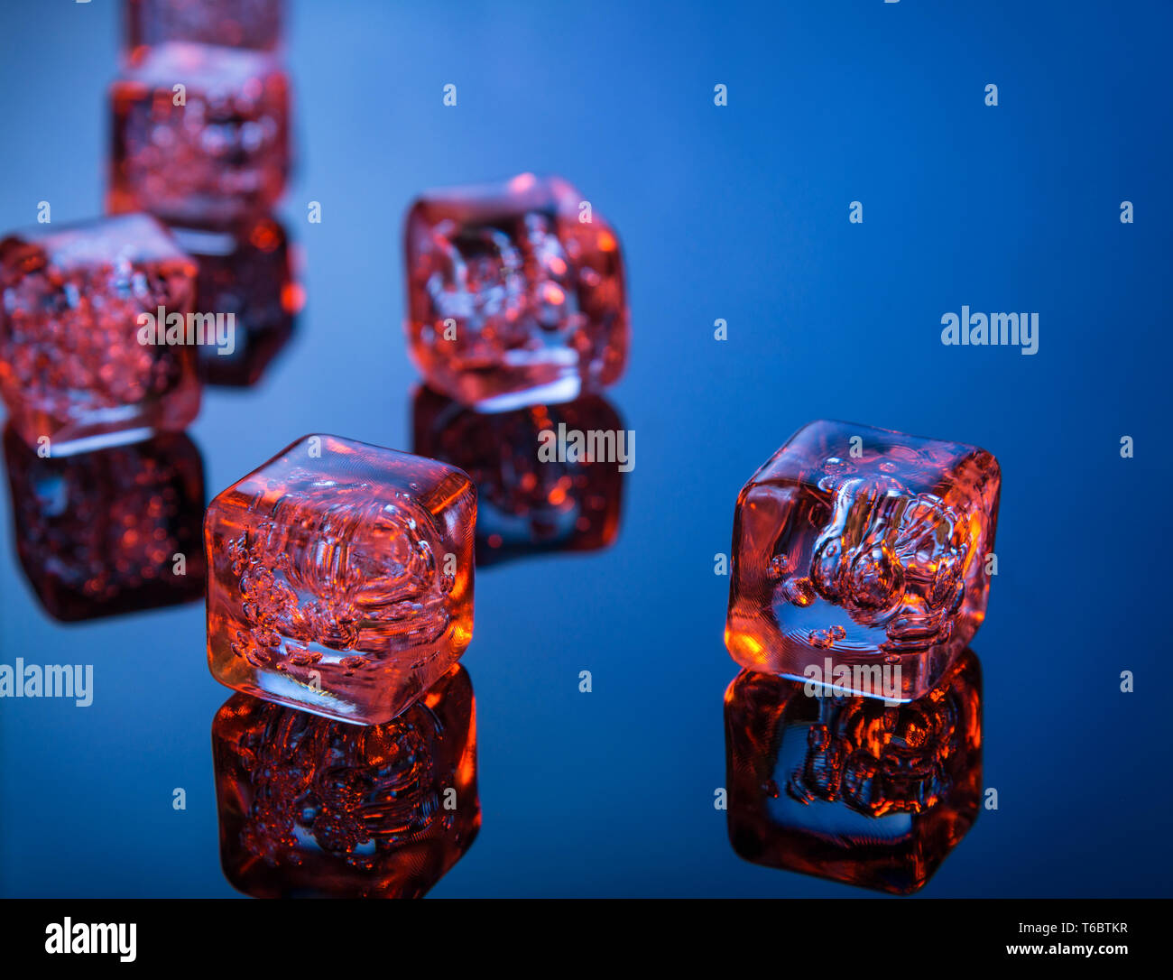 Glowing ice cubes on blue reflective surface Stock Photo