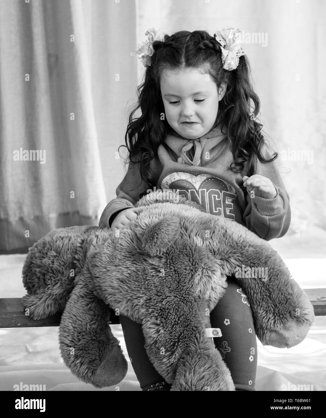 Angry little girl beating her teddy bear - domestic abuse concept. Girl 4-5 year old punishes toy bear. Stock Photo