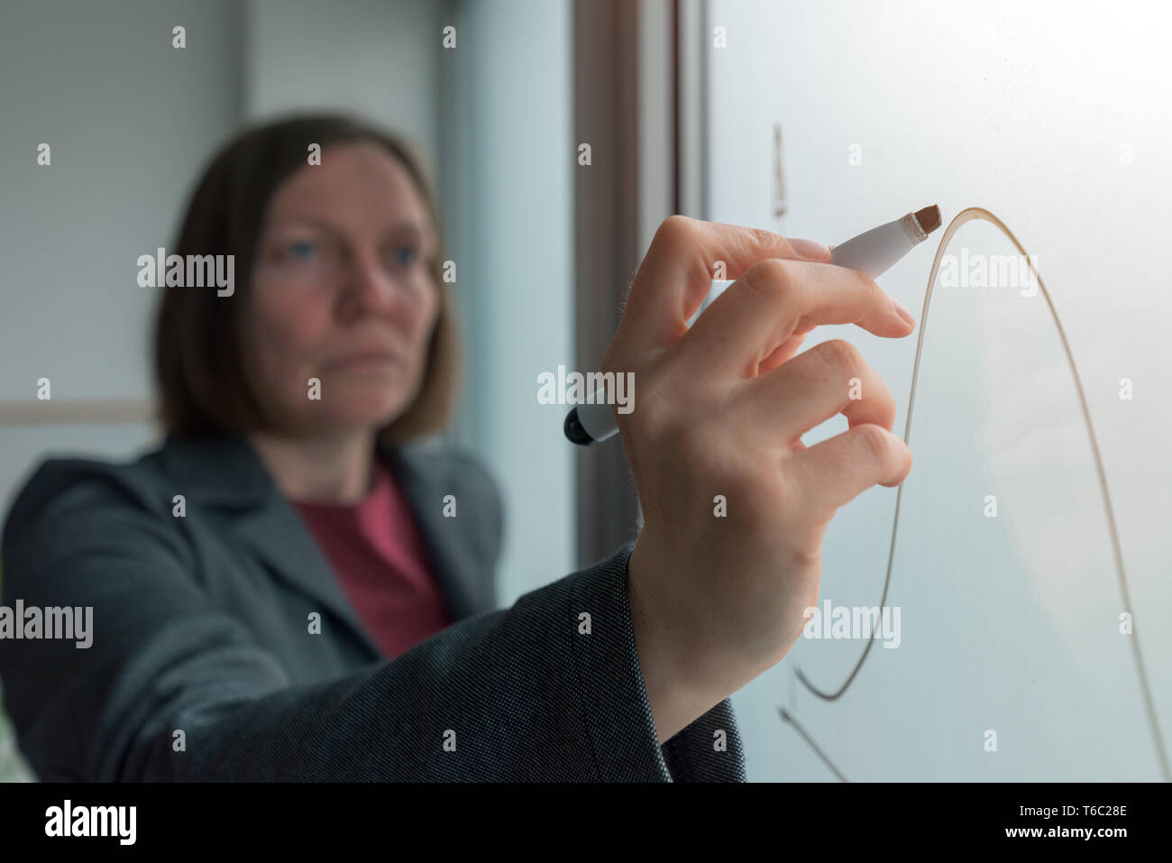 Businesswoman drawing graph on whiteboard in office while presenting business results during corporate meeting Stock Photo