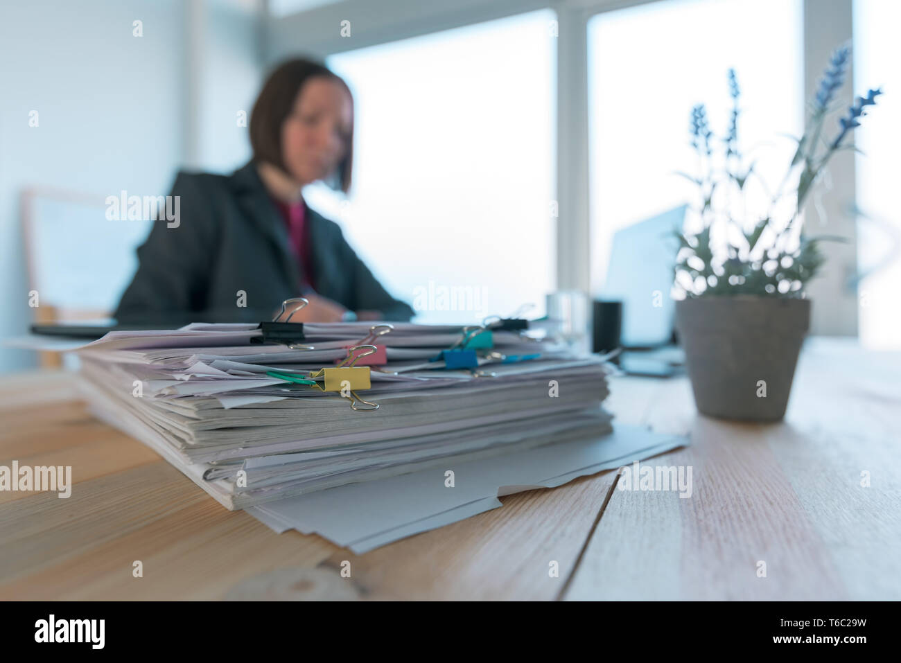 Busy businesswoman doing paperwork in office at the desk filled with papers and documentation Stock Photo
