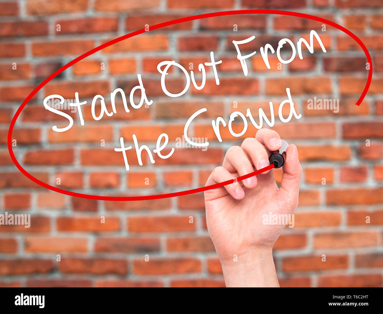 Man Hand writing Stand Out From the Crowd with black marker on visual screen Stock Photo