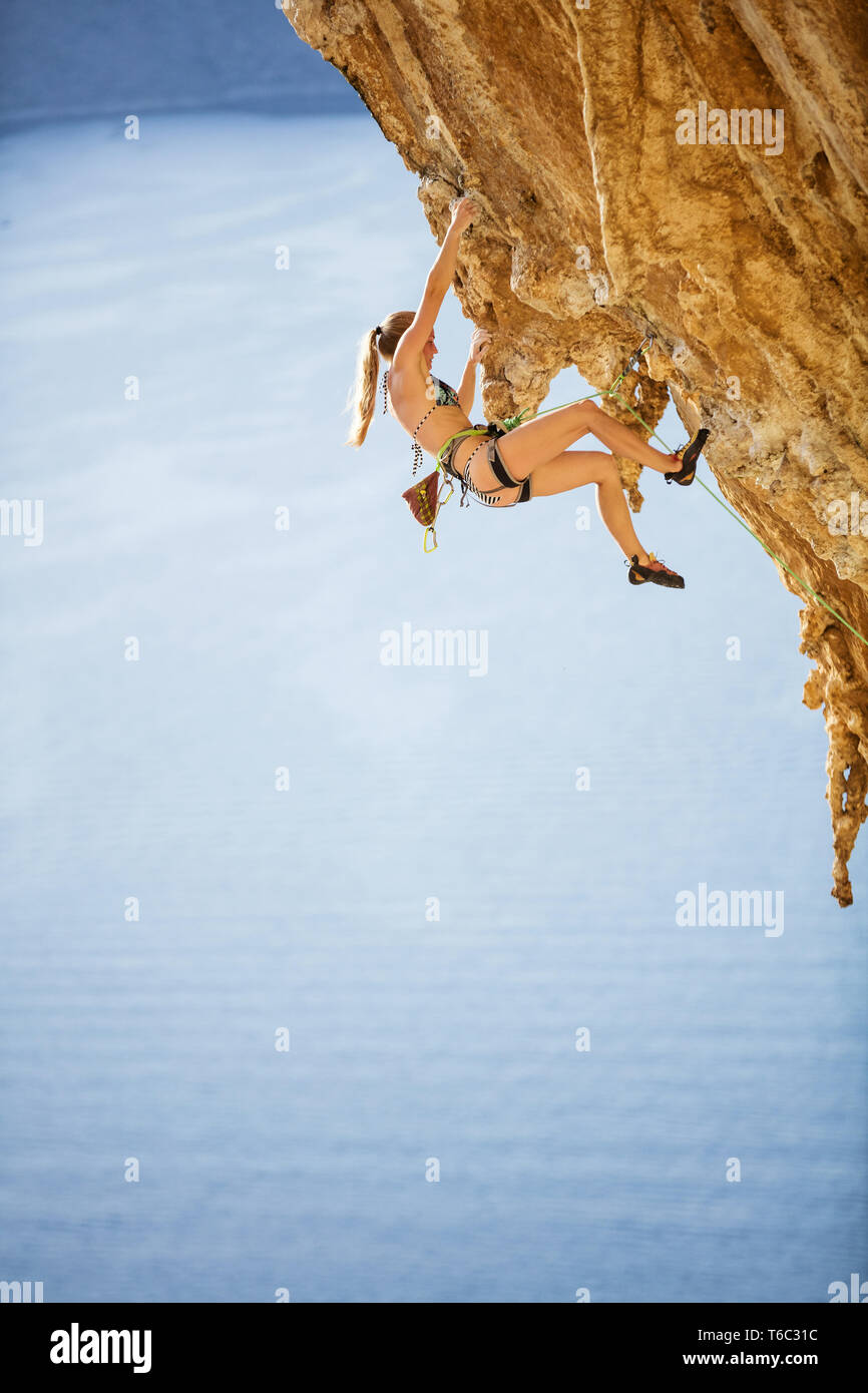 Caucasian young woman in bikini climbing challenging route on