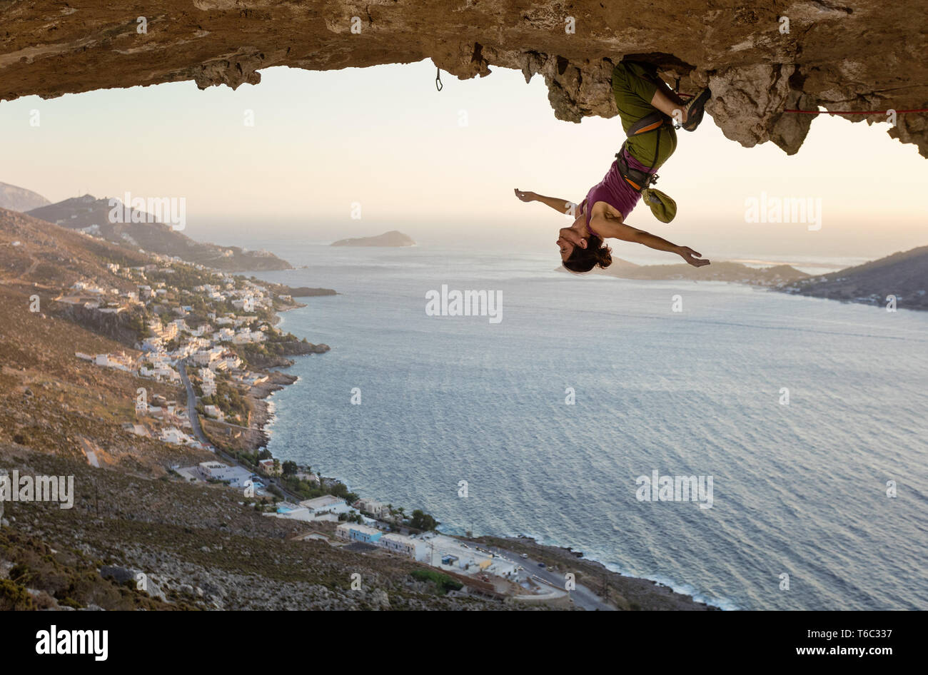 Female rock climber hanging upside down on challenging route in cave at