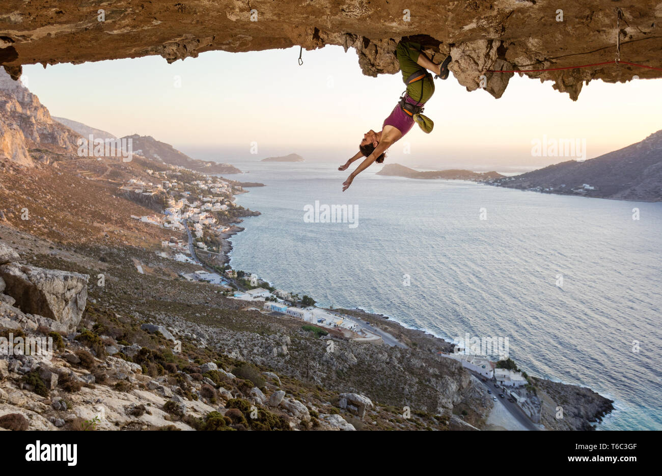 Female rock climber hanging upside down on challenging route in cave at