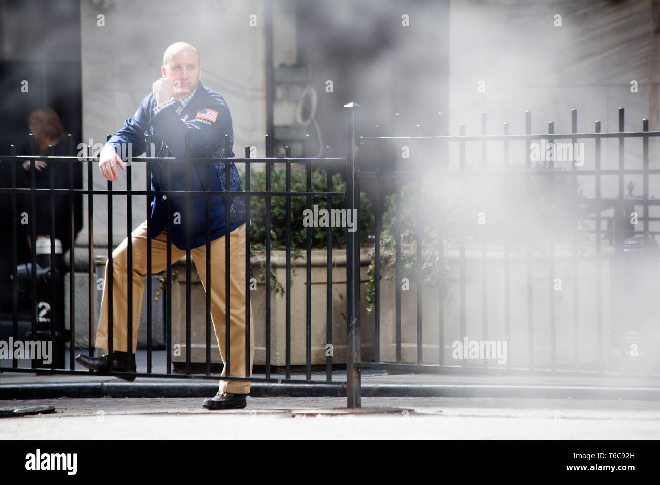 A floor trader takes a cigarette break outside tne NYSE Euronext Stock Exchange on Wall Street. He is halfway hidden by the steam leaking from the underground steam power pipes that provide many Manhattan office buildings with cooling power. Stock Photo