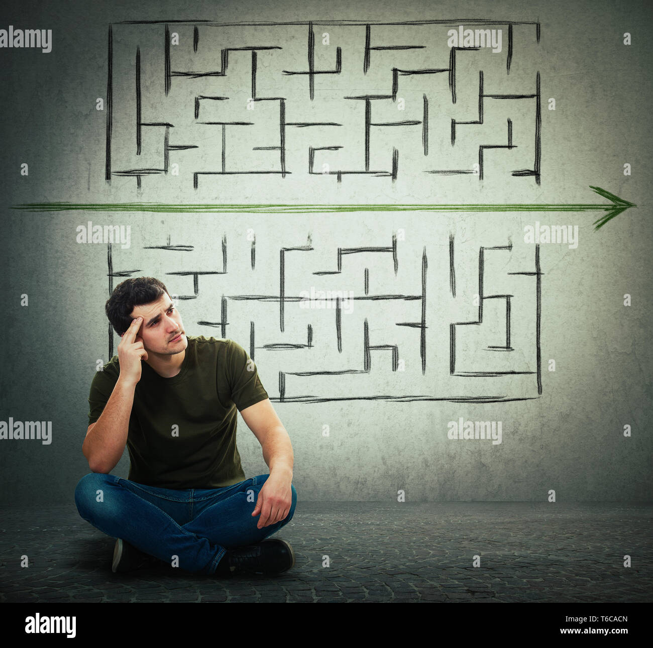 Man sitting on the floor hard thinking, find a solution to solve problem and escape from labyrinth. Breaking the rules, as a green arrow pierce the ma Stock Photo