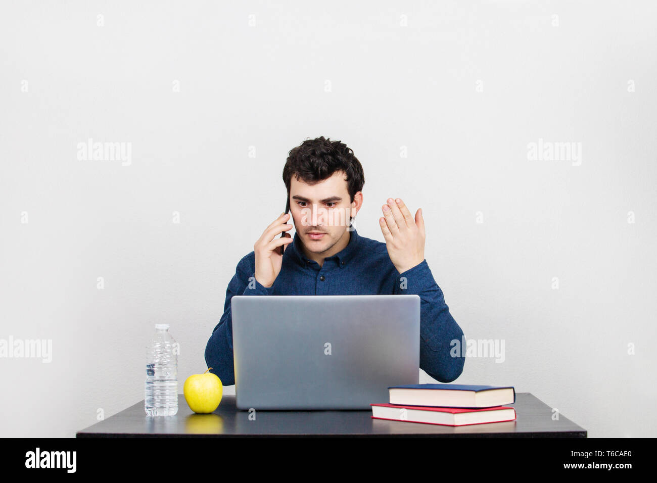 Frustrated young businessman sitting on chair talking on his mobile phone. Unhappy casual guy receiving bad news on the telephone isolated over white. Stock Photo