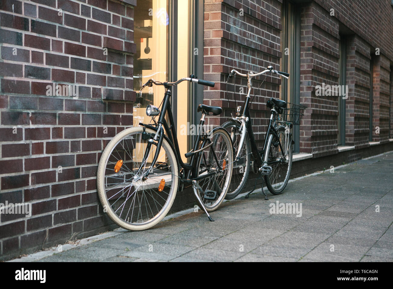 Bicycles are parked next to a brick wall of a building on a city street. Stock Photo