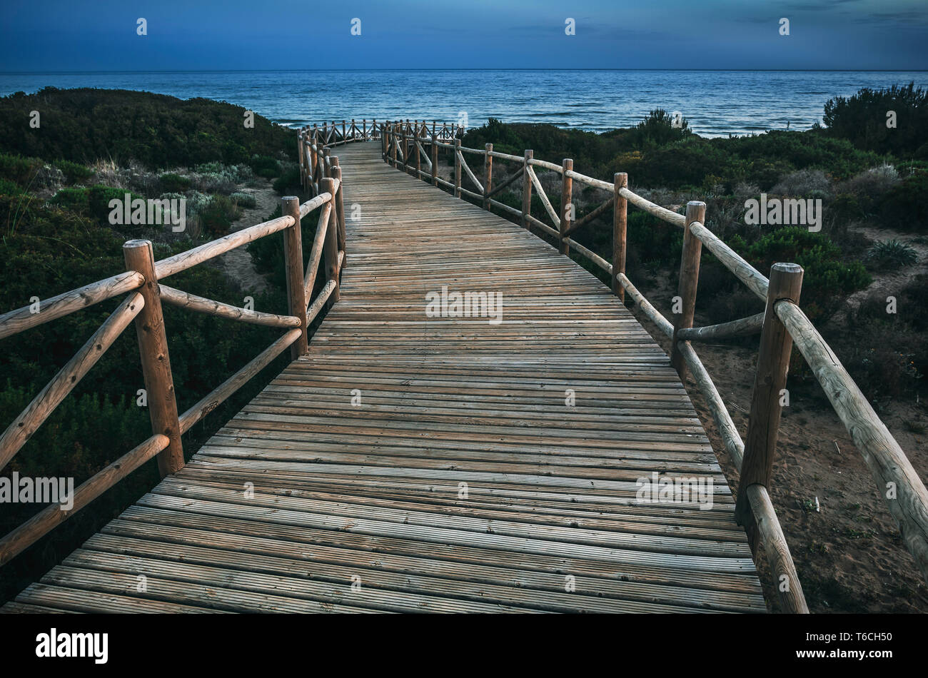 Lumber pathway leading to rippling sea on tranquil evening in countryside in Cabopino, Artola dunes. Marbella, Spain Stock Photo