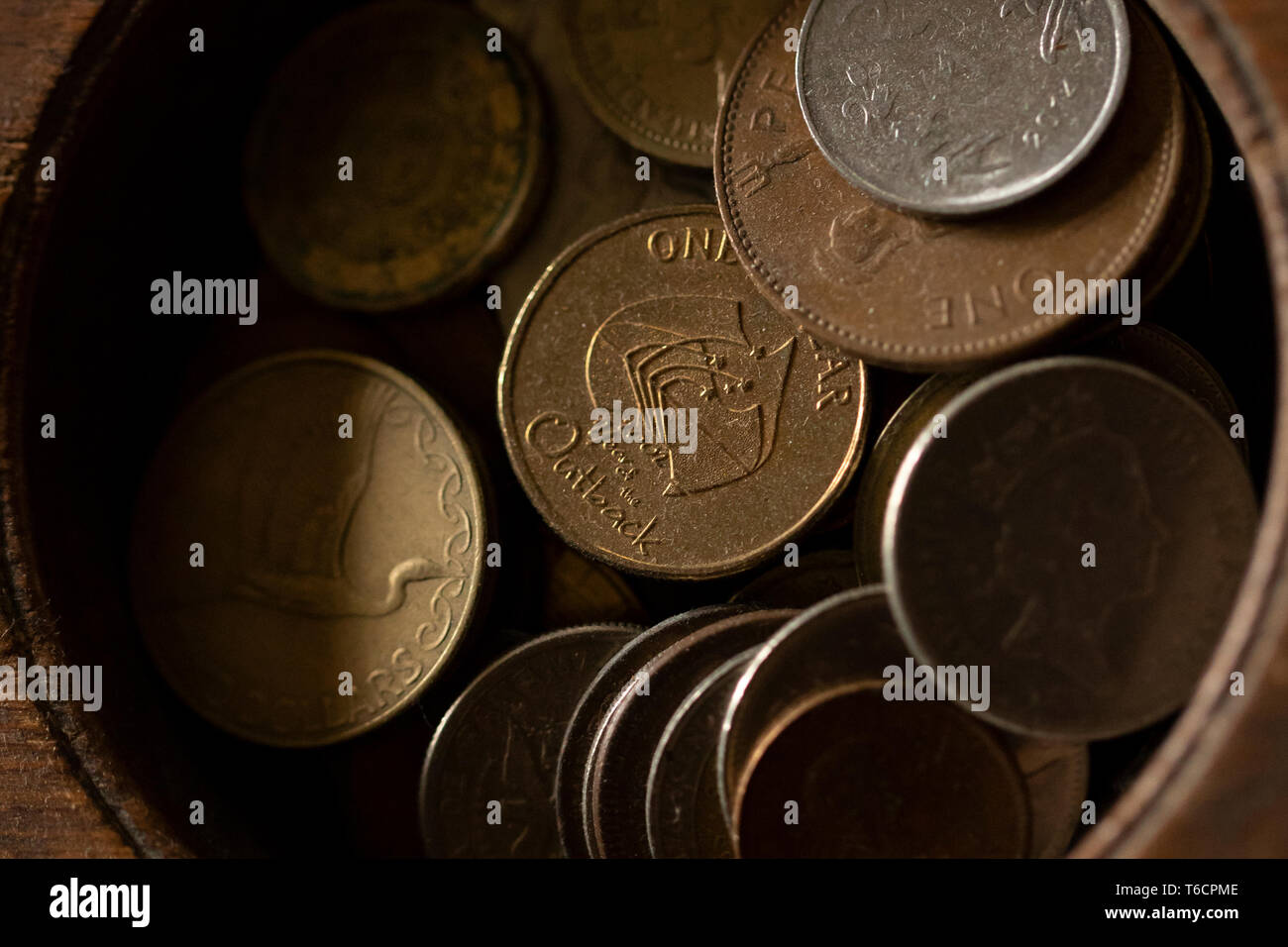 A wooden container full of foreign coins, including currency from Australia, Greece, and the United Kingdom. Stock Photo